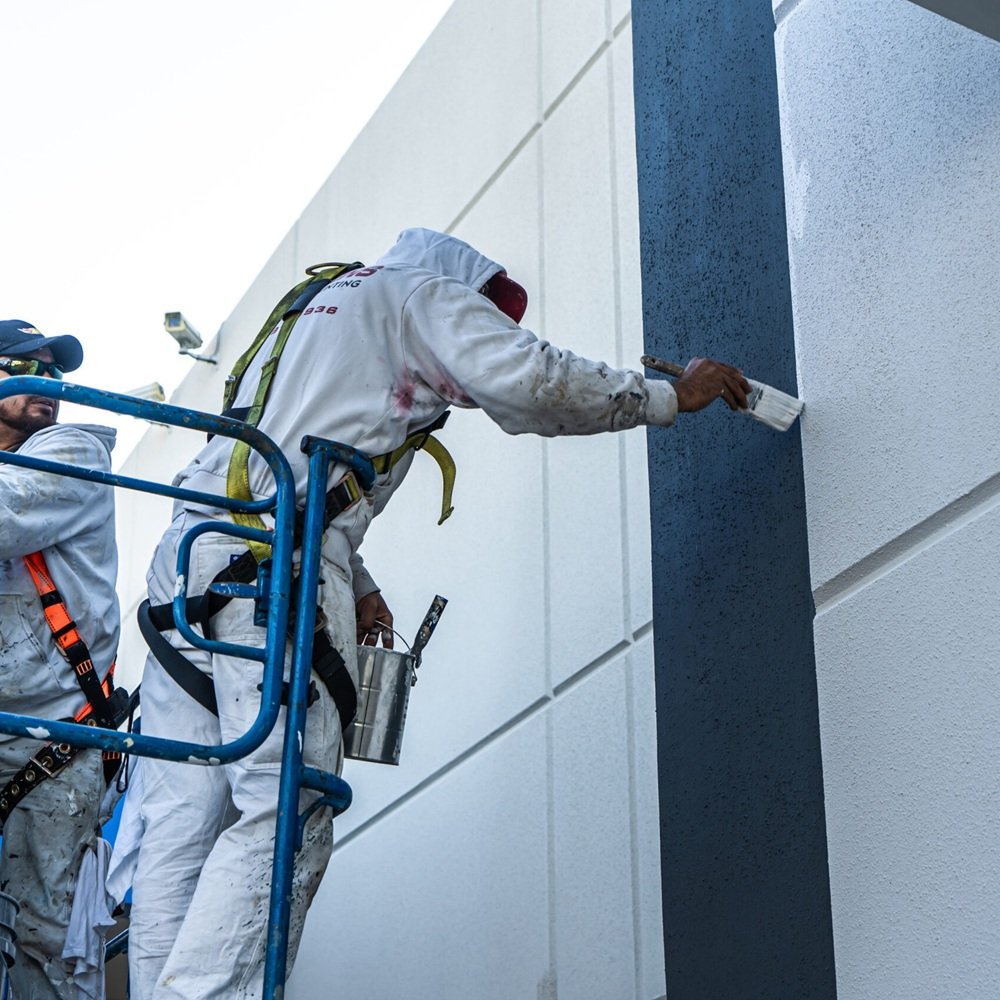 Crew repainting commercial storefront exterior while protecting entry doors and sidewalks