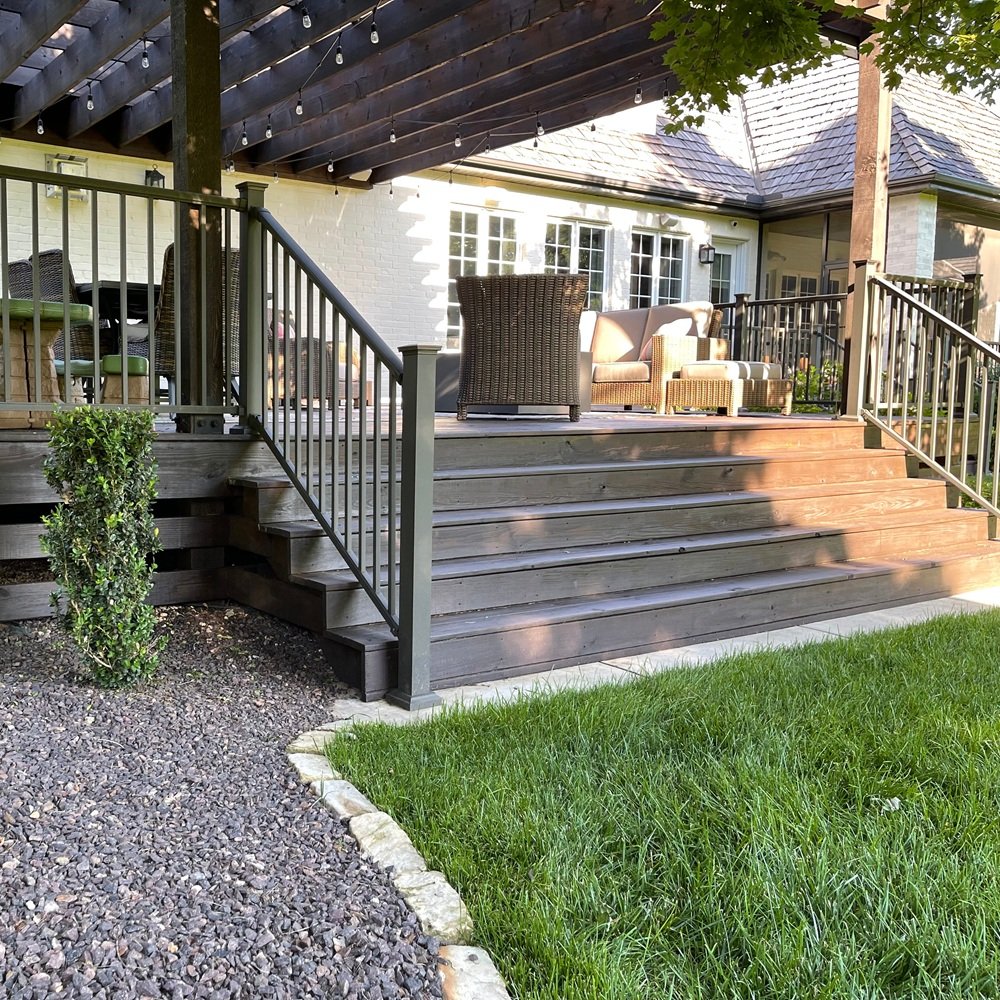 Fresh stain being applied to a backyard deck beside an occupied home